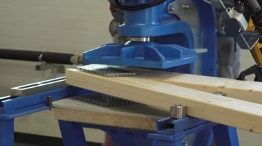 Balvi, Letonya - 25 Mayıs 2024 - Metal levhaları ahşap kirişlere bastıran makine, bir atölyede endüstriyel doğrama işlemini gösteriyor.