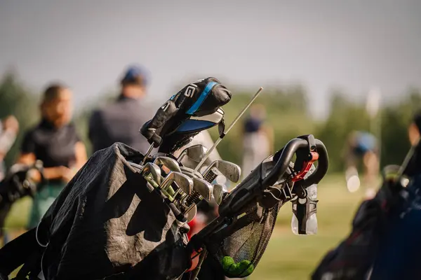 Valmiera, Letonya - 1 Haziran 2024 - Golf sahasında güneşli bir günde arka planda bulanık oyuncuların olduğu bir çantada golf sopaları.