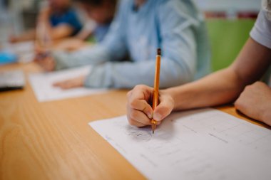 Valmiera, Letonya - 22 Mayıs 2024 - Arka planda çalışan sınıf arkadaşlarıyla birlikte, bir öğrencinin el yazısına kağıt üzerine kalemle yakın çekim.