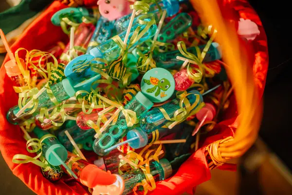 Valmiera, Letonya - 31 Mayıs 2024 - Baloncuklu değnekler ve kurdele süslemeleri ile dolu renkli bir sepet, şirin tasarımlar, sıcak ışıklandırma altında, bir çocuk partisi için hazır.