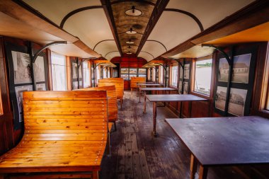 Dobele, Letonya - 7 Haziran 2024 - Duvarlarında tarihi fotoğraflar ve sıcak, nostaljik bir atmosfer bulunan ahşap bankları ve masaları olan klasik bir tren vagonunun içi.