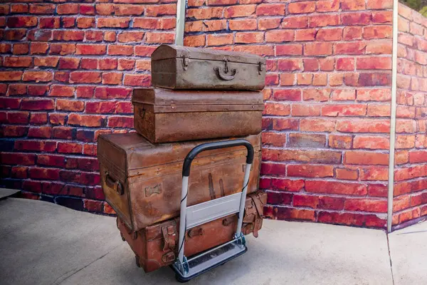 stock image Dobele, Latvia - June 7, 2024 - Stack of three vintage suitcases on a hand truck against a brick wall background, creating a nostalgic travel theme.