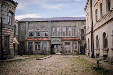 Dobele, Letonya - 7 Haziran 2024 - Temiz bir gökyüzü altında eski, yıpranmış binalarla çevrili terk edilmiş bir kaldırım taşı avlusu.