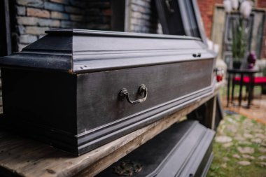 Dobele, Letonya - 7 Haziran 2024 - Metal saplı siyah ahşap bir tabut, tuğla ve taştan oluşan bulanık bir zemine yerleştirilmiş..