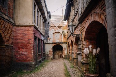 Dobele, Letonya - 7 Haziran 2024 - Eski tuğlalı binalarla kaplı dar, kaldırımlı bir ara sokak, kemerli kapılar ve klasik fenerler, tarihi ve kırsal bir ortam yaratıyor..