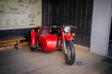 Dobele, Letonya - 7 Haziran 2024 - Ahşap zeminde, duvarın yanında bir harita ve bankın yanına park etmiş eski model bir motosiklet.