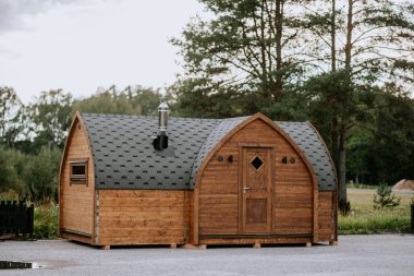 Tahta bir kulübe, kiremitli bir çatı, küçük pencereler ve arka planda ağaçlar olan bir baca. Kırsal ve samimi bir görüntüsü var..