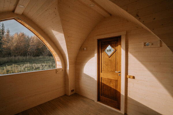 Wooden interior with an arched window offering a scenic outdoor view and a wooden door. Warm natural light fills the space.