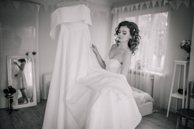 Valmiera, Letonya - 9 Eylül 2023 - Gelin, beyaz gelinliğini büyük bir pencere ve aynalı bir odada tutuyor, siyah ve beyaz olarak yakalandı..