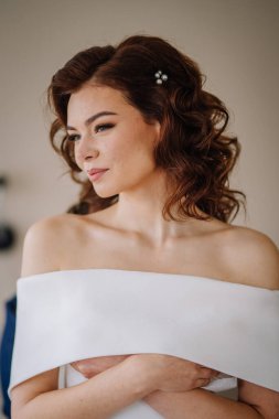 Valmiera, Latvia - September 9, 2023 - A bride with curled hair and pearl hairpins, wearing an off-the-shoulder white dress, looking to the side with a serene expression. clipart