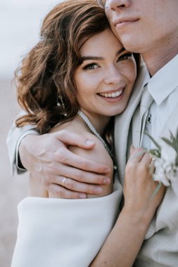 Valmiera, Letonya - 9 Eylül 2023 - Damat tarafından kucaklanan gülümseyen bir gelinin yakın çekimi, plajdaki düğün günlerinde sevgi, neşe ve samimiyet gösterisi.