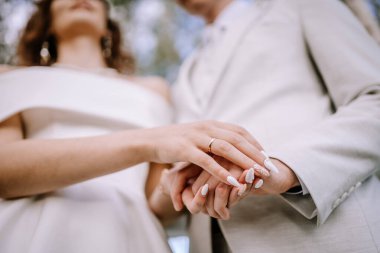 Valmiera, Letonya - 9 Eylül 2023 - Gelin ve damadın el ele tutuşup iç içe geçmiş parmaklarına ve nikah yüzüklerine odaklandıkları, gelinin ön plandaki detaylı tırnaklarıyla düşük açılı çekim.