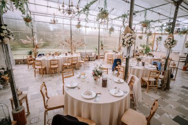 Valmiera, Letonya - 9 Eylül 2023 - Yuvarlak masalar, zarif çiçek süslemeleri ve geniş bir mekanda dekoratif avizeler ile güzel bir düğün resepsiyonu.