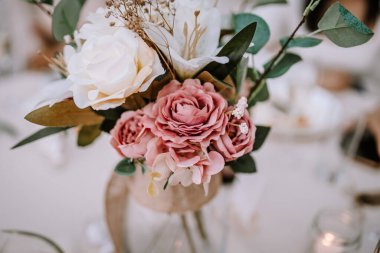 Valmiera, Letonya - 9 Eylül 2023 - Beyaz ve pembe güllerin, yeşil yaprakların ve dekoratif elementlerin yer aldığı bir çiçek düzeninin yakın çekimi.