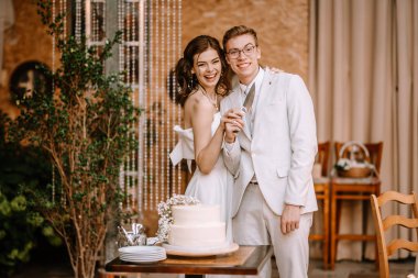 Valmiera, Letonya - 9 Eylül 2023 - Bir gelin ve damat, bebek nefesli çiçeklerle süslenmiş düğün pastalarını kesmeye hazır bir pasta bıçağıyla mutlu bir şekilde poz verirler..