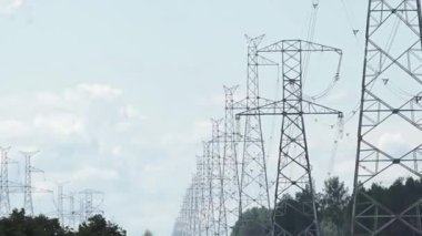 Yüksek voltajlı elektrik hattı kuleleri, bulutlu bir gökyüzünün altındaki ağaçlarla kırsal bir alana yayılarak elektrik altyapısını gösteriyor..