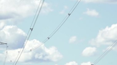 Yüksek voltajlı elektrik hatları bulutlu bir gökyüzü boyunca uzanıyor, kablolar ve uzaylıları mavi gökyüzü ve bulutların arkaplanına karşı detaylı bir şekilde gösteriyor..