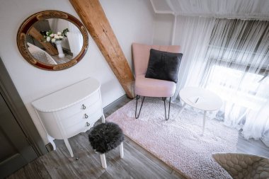 Blome, Letonya - 11 Eylül 2023 - Pembe koltuklu rahat bir köşe, siyah yastık, beyaz yan masa, yuvarlak ayna ve tavan arası yatak odasında küçük pofuduk bir tabure.