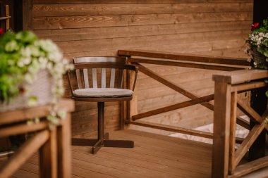 Blome, Letonya - 11 Eylül 2023 - Ahşap minderli ahşap bir verandada, ahşap bir korkuluk ve rahat, kırsal bir yerde saksı bitkisi ile oturmaktadır..