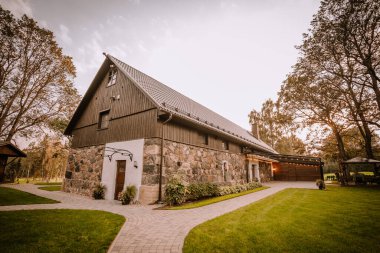 Blome, Letonya - 11 Eylül 2023 - Taştan ve ahşap cepheli taştan bir ev, temiz bir gökyüzü altında yemyeşil çimenler, ağaçlar ve patikalarla çevrili, sakin bir atmosfer yaratıyor. Boşluğu kopyala.