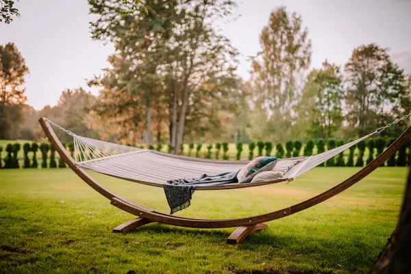 Stock image Blome, Latvia - September 11, 2023 - A hammock with pillows and a blanket on a green lawn, surrounded by trees and bushes, creating a peaceful outdoor relaxation spot. Copy space.