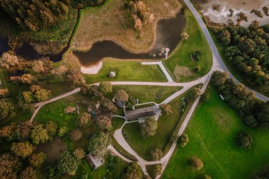 Blome, Letonya - 11 Eylül 2023 - Ev, patika, ağaçlar, gölet ve kumlu sahil manzaralı kırsal bir arazinin havadan görünüşü.