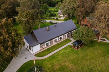 Blome, Letonya - 11 Eylül 2023 - Çimleri, bahçeleri ve ağaçları iyi korunmuş, açık tente oturma alanı olan bir verandası olan büyüleyici bir evin havadan görünüşü.