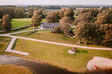 Blome, Letonya - 11 Eylül 2023 - Geniş çimenli, havuzlu, taraçalı ve güneşli bir günde etrafı ağaçlarla çevrili kırsal bir arazinin havadan görünüşü.