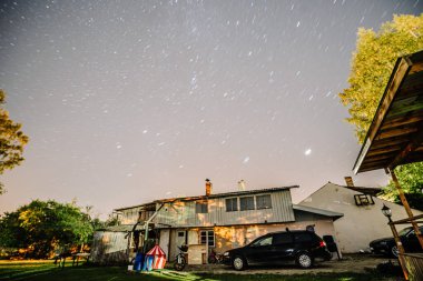 Valmiera, Letonya - 15 Eylül 2023 - Dışarıda arabaların park ettiği kırsal bir ev, bir çadır ve açık yıldızlı bir gökyüzü. Boşluğu kopyala.