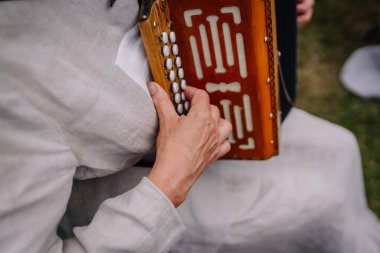limbazi, Letonya, 29 Haziran 2024 - Bir insanın akordeon çaldığı yakın plan, düğmelere odaklanma ve karmaşık ahşap işçiliği. Geleneksel kıyafetler giyiyor..
