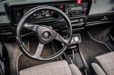 limbazi, Letonya, 29 Haziran 2024 - VW logosu, gösterge paneli kontrolleri ve kareli koltukları olan siyah bir direksiyonun yakın çekimi.