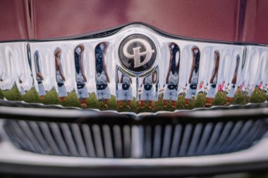 limbazi, Letonya, 29 Haziran 2024 - Krom kaplamalı klasik bir araba ızgarasına yakın çekim, yakınlarda duran insanları yansıtıyor, arabanın amblemi merkezde..