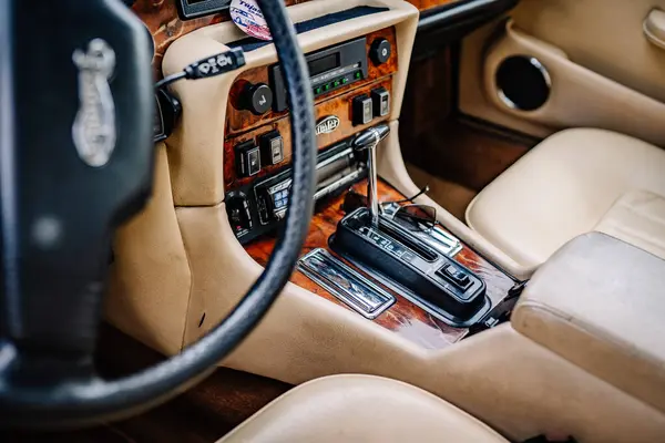 stock image limbazi, Latvia, June 29, 2024 - Close-up of a vintage car's interior, focusing on the steering wheel, gear shift, wood paneling, and beige leather seats.