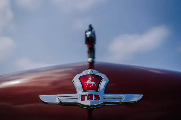 stock image limbazi, Latvia, June 29, 2024 - Close-up of a red vintage car's hood with a GAZ emblem featuring a chrome deer ornament against a blue sky background.