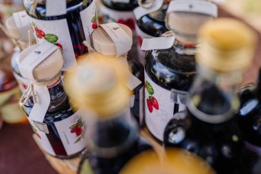 limbazi, Letonya, 29 Haziran 2024 - Ahşap kapaklı çeşitli meyve likörü şişeleri ve açık hava pazarında sergilenen resimli etiketler, sanatsal içeceklerin altını çiziyor.