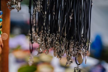 limbazi, Latvia, June 29, 2024 - Close-up of assorted silver pendants and charms hanging on black leather cords, displayed for sale at a market or craft fair. clipart