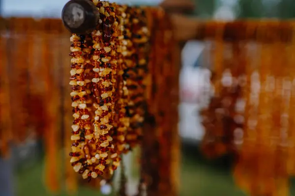 stock image limbazi, Latvia, June 29, 2024 - Close-up of amber necklaces hanging from a wooden display at a market, showcasing the rich, warm hues of the amber beads.