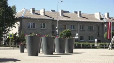 Balvi, Letonya - 28 Mayıs 2024 - Letonya Balvi, Letonya 'da güneşli bir günde büyük saksıları ve Letonya bayrak süslemeleri olan bir konut binasının videosu.