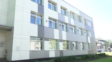 Balvi, Letonya - 28 Mayıs 2024 - Büyük pencereli modern bir binanın videosu ve güneşli bir günde girişte duran bir kız. Boşluğu kopyala.