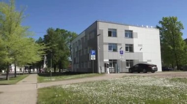 Balvi, Letonya - 28 Mayıs 2024 - Güneşli bir günde elektrikli araç şarj istasyonu, park levhası ve çevreleyen yeşil alanı olan modern bir binanın videosu. Boşluğu kopyala.