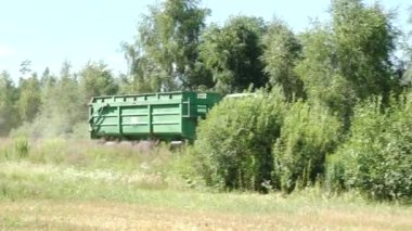 Valmiera, Letonya - 9 Temmuz 2024 - Güneşli bir günde yemyeşil ve ağaçlarla çevrili yemyeşil bir tarladan geçen karavanı olan yeşil bir traktör.