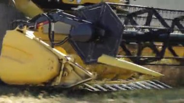 Valmiera, Letonya - 9 Temmuz 2024 - Bir biçerdöver başlığının hareket halindeki metal parçaları ve sarı bileşenleriyle bir arpa tarlasını keserek yakın plan görüntüsü.