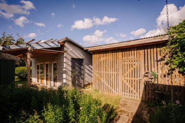 Valmiera, Letonya - Temmuz - 5, 2024 - Kırsal ahşap bir kulübe ve pergola ile çevrili, parlak mavi gökyüzü altında tüylü bulutlarla çevrili bitmemiş bir bina.