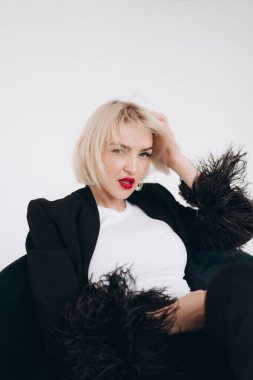 Siyah ceketli şık bir kadın. Tüylü kolları, beyaz bluzu ve kırmızı ruju var. Yakın plan bir portrede kendine güveni ve zarafeti var..