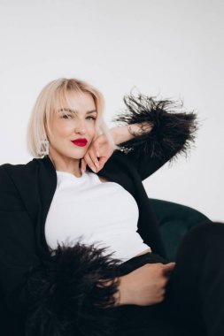 Siyah ceketli şık bir kadın. Tüylü kolları, beyaz bluzu ve kırmızı ruju var. Yakın plan bir portrede kendine güveni ve zarafeti var..