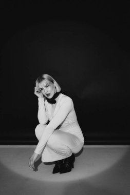 Şık bir kadının siyah-beyaz portresi. Sarışın, kısa saçlı, kırmızı rujlu. Hafif bir elbise ve siyah boyunlu bir aksesuar içinde çömelmiş. Boşluğu kopyala.