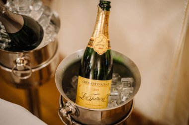 Riga, Letonya 20 Mart 2024 - Buz kovalarında soğutulmuş Crmant d 'Alsace şişeleri, beyaz masa örtüsü ile hazırlanmış, kutlamaya hazır