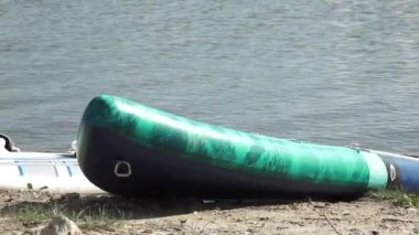 Valmiera, Letonya - 29 Temmuz 2024 - Yeşil şişme bir kürek sakin suların kumlu kıyısında duruyor, açık deniz aktiviteleri için huzurlu bir ortam olduğunu gösteriyor.