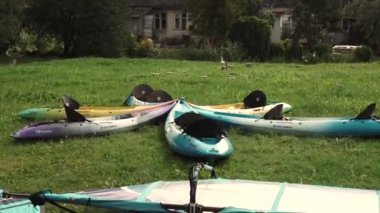 Valmiera, Letonya - 29 Temmuz 2024 - Bir evin yakınındaki çimenli bir alanda çeşitli renkli kanolar düzenlenir, bu da açık hava su aktivitelerine duraklama veya hazırlık anlamına gelir..