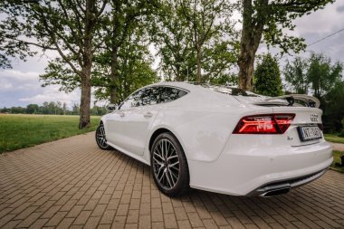 Valmiera, Letonya - 1 Ağustos 2024 - Asfaltlı bir yolda park etmiş beyaz bir Audi A7 'nin arka-yan görüntüsü, gösterişli tasarımı, arka lambaları ve ağaçlar ve yeşilliklerle çevrili çevresi.